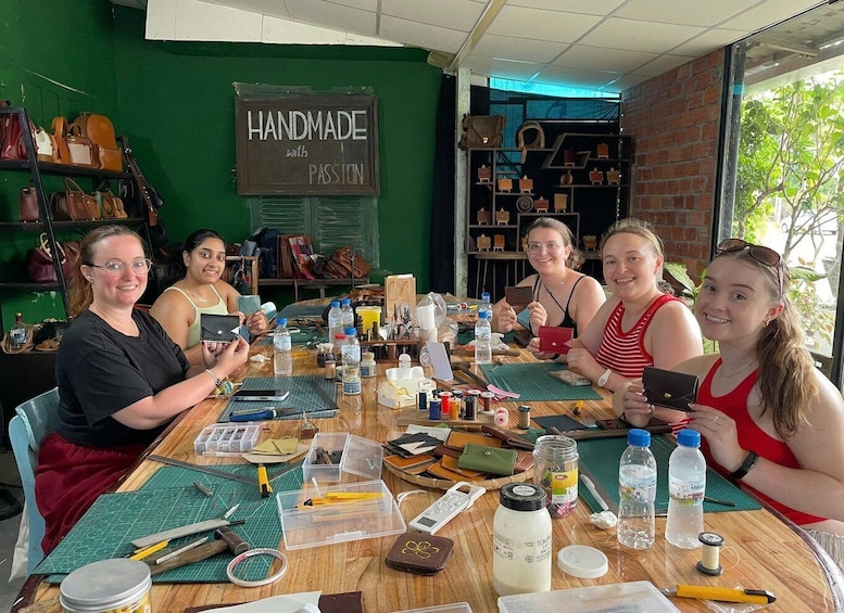 A group of people at a table with crafting supplies, surrounded by handbags and a 'Handmade with Passion' sign. 1