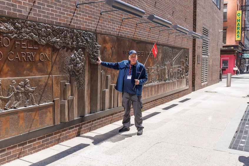 A man pointing at a bronze plaque with inscriptions and reliefs on a brick wall. 2
