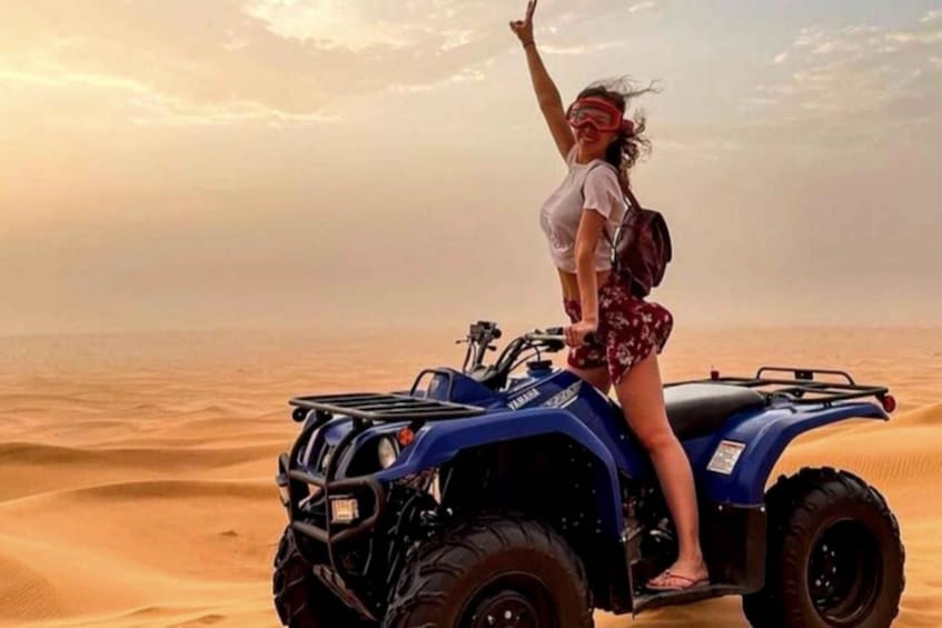A person standing on a blue ATV in a desert with sand dunes. 5