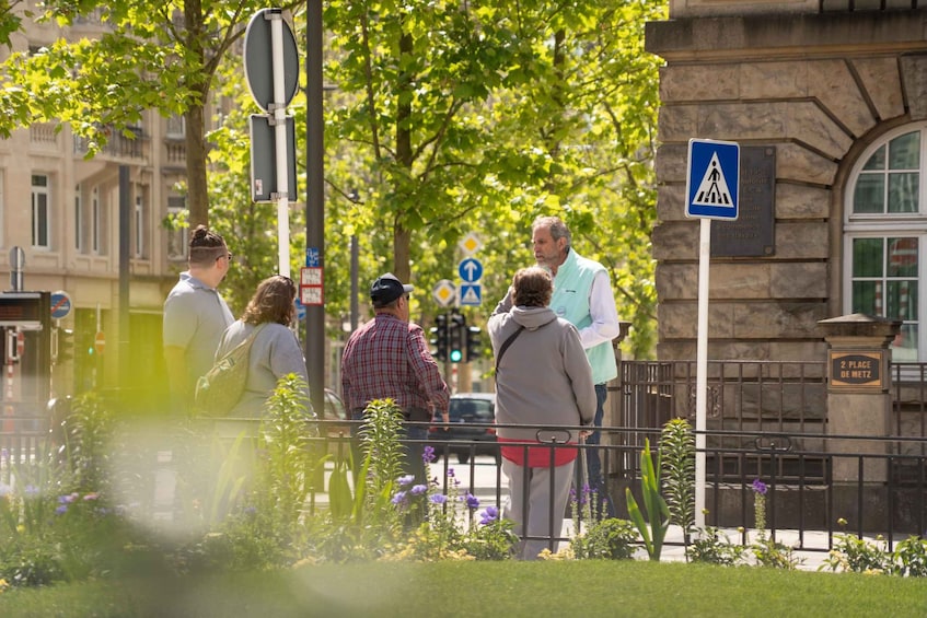 A group of people standing by a fence with a pedestrian crossing sign and a building with a plaque. 2