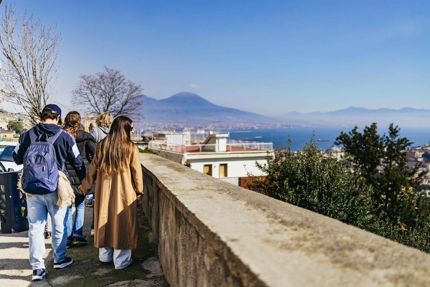 A group of people walking along a stone wall overlooking a city with a mountain in the distance. 1