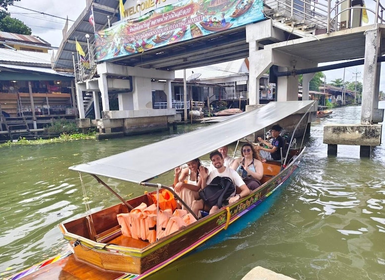 A traditional long-tail boat with passengers on a river, under a bridge with a colorful welcome sign. 4