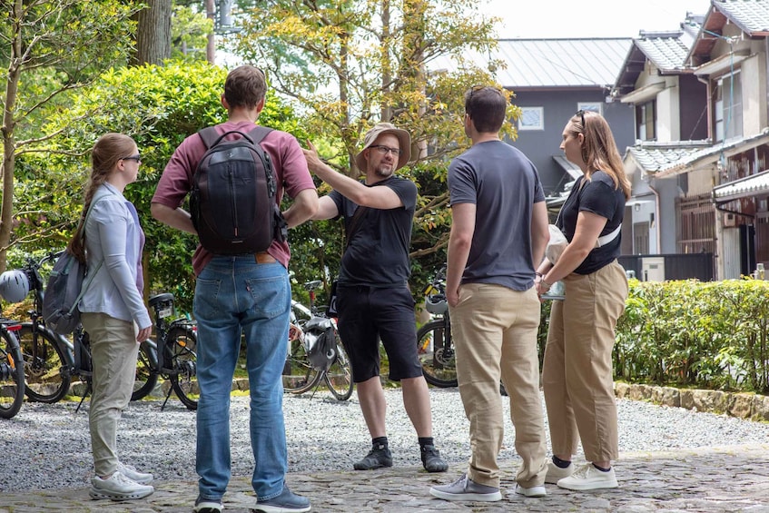 Un groupe de personnes se tient sur un chemin pavé de pierres, avec des vélos garés à proximité, entouré de verdure et de bâtiments traditionnels. 4