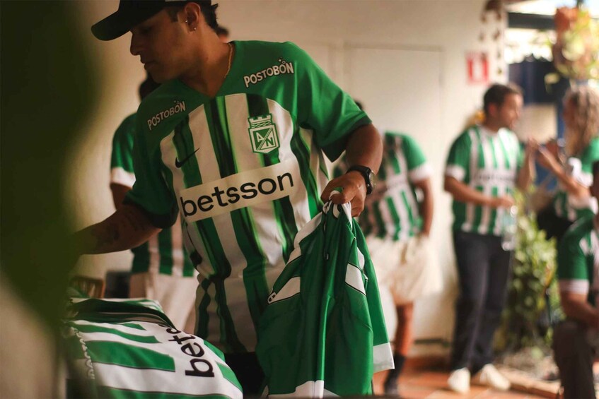 A person in a green and white striped jersey holding a bag, with another individual in a similar jersey in the background. 4