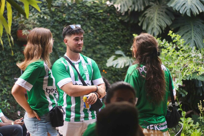 People in green and white striped jerseys, likely at a sports event, with lush greenery in the background. 5