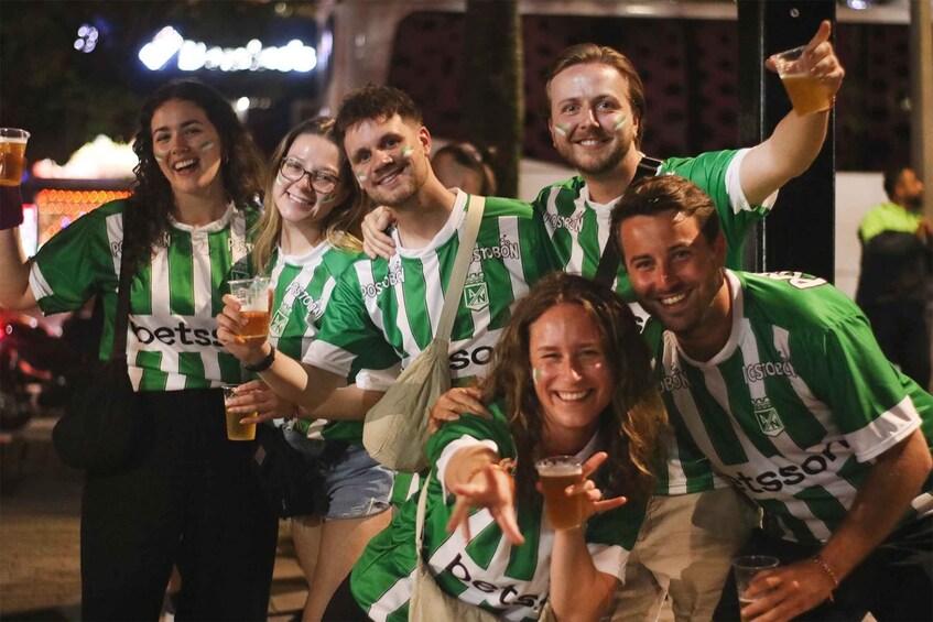 A group of people in green and white striped jerseys, holding drinks, and posing for a photo. 2