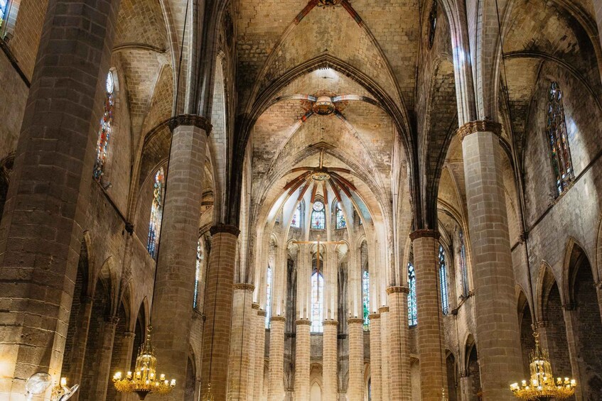 A cathedral interior with high vaulted ceilings, large stained glass windows, and multiple chandeliers. 3