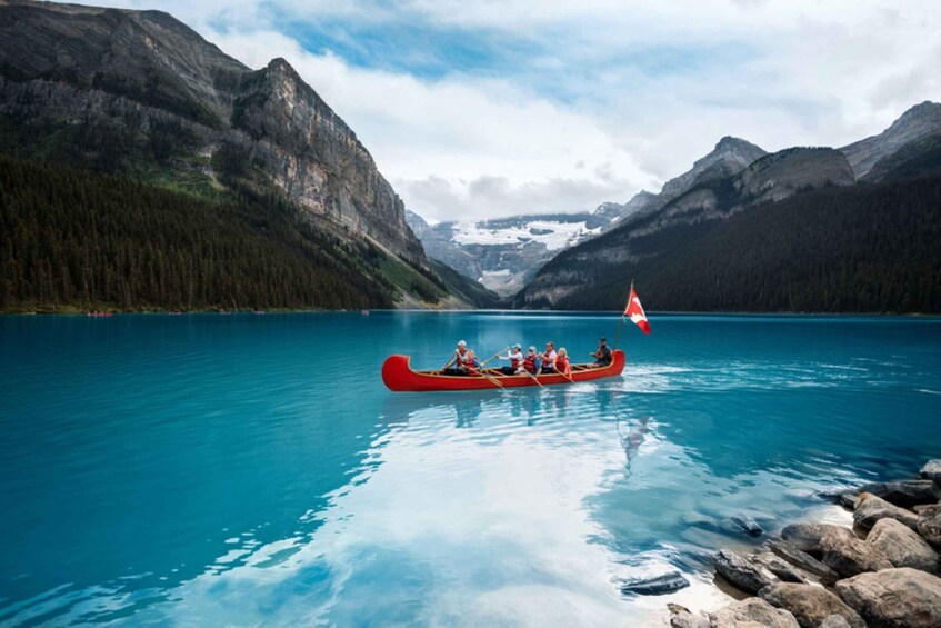 A red canoe with people rowing on a calm lake surrounded by mountains. 3