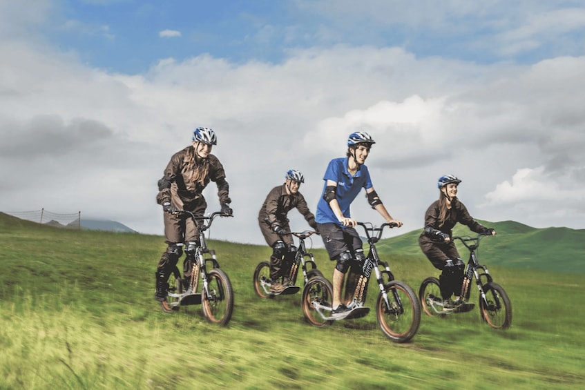 Vier Personen fahren auf Mountainbikes über eine Wiese mit Hügeln im Hintergrund. 5