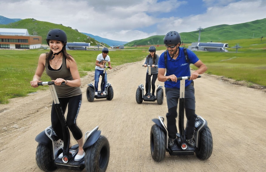 Vier Personen fahren mit Segways auf einer unbefestigten Straße, im Hintergrund grüne Hügel. 4