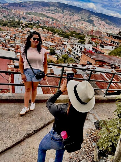 A person taking a photo of a cityscape with buildings and mountains in the background. 5