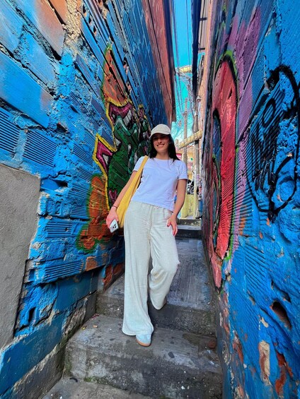 A person standing on a narrow street with colorful graffiti on the walls. 4