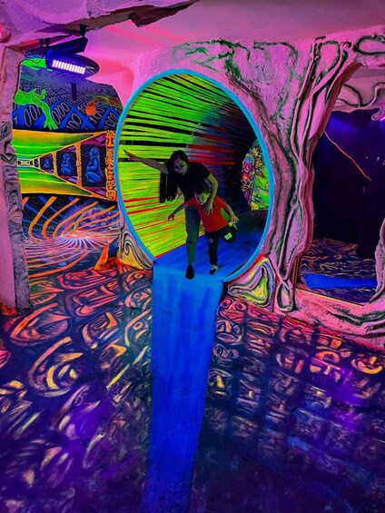 A person and a child in a colorful, illuminated tunnel with artistic murals. 5