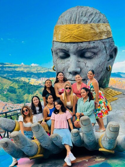 A group of people posing with a large stone statue of a face, set against a cityscape. 3