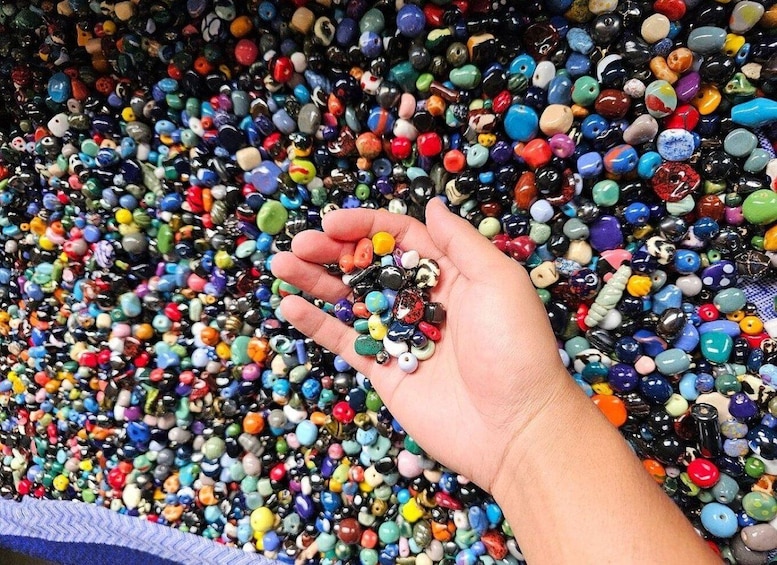 Eine Hand hält verschiedene farbige Perlen vor einer großen Sammlung von Schmuckperlen. 5