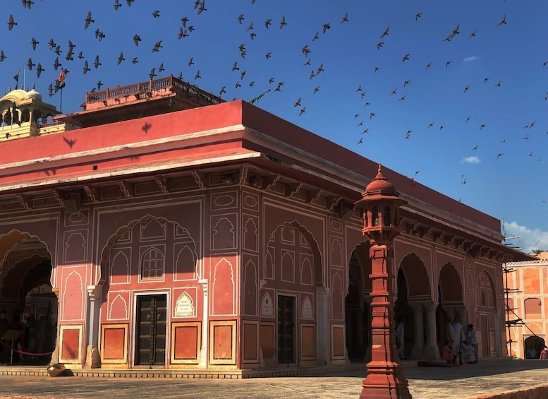 A historic building with intricate architecture and a large number of birds flying in the sky. 2