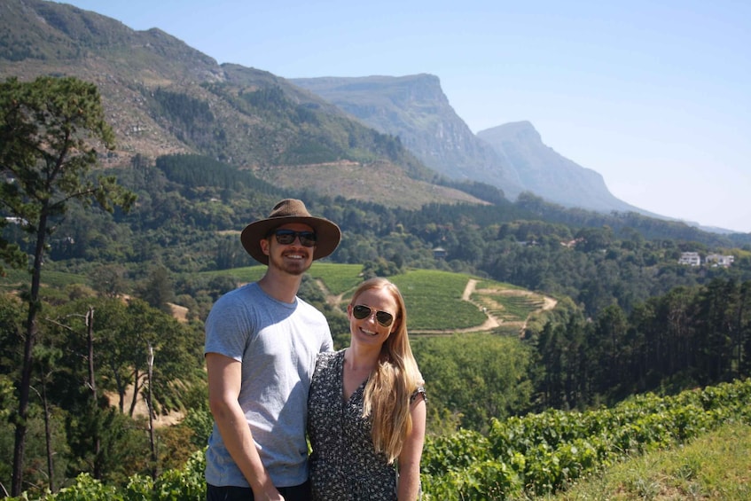A couple standing in a vineyard with mountains in the background. 3