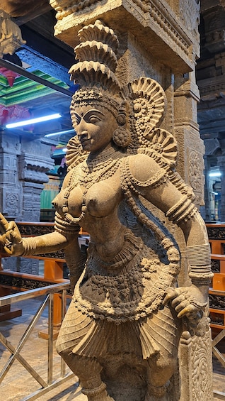 A detailed stone sculpture of a deity with elaborate jewelry and a headdress, set against a backdrop of a temple interior with stone railings and architectural elements. 2