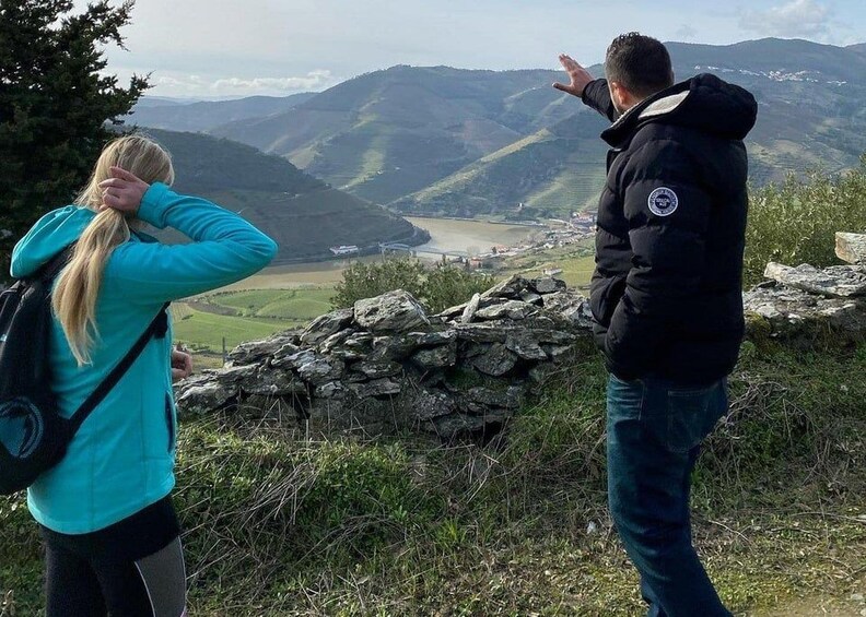 Två personer står på en klippavsats och blickar ut över en dal med en flod och avlägsna berg. 5