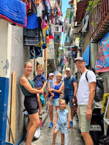 A narrow alleyway with colorful clothes hanging on lines, a motorcycle parked on the right, and a group of people standing and posing for the photo. 2