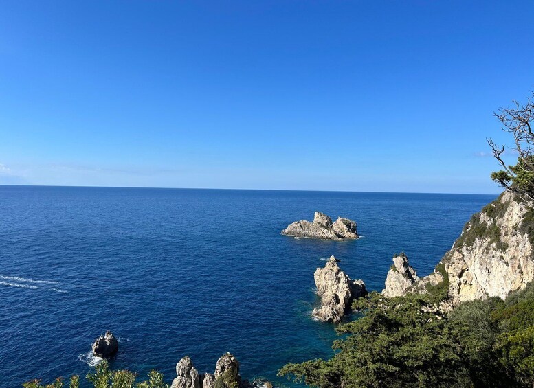 A coastal landscape with clear blue sea, rocky outcrops, and dense greenery. 2