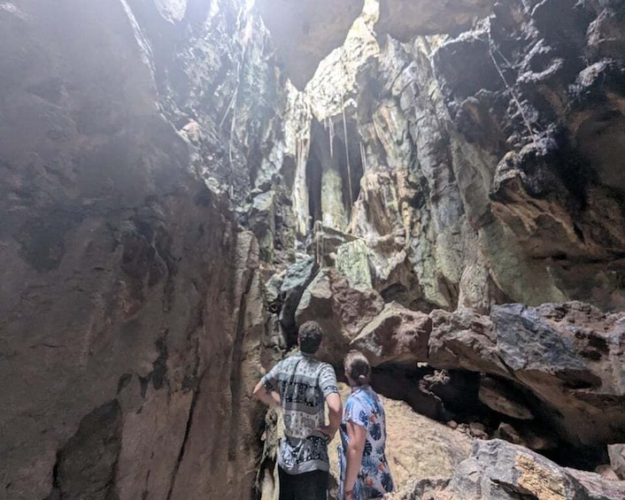 Two people exploring a rocky cave with stalactites. 1