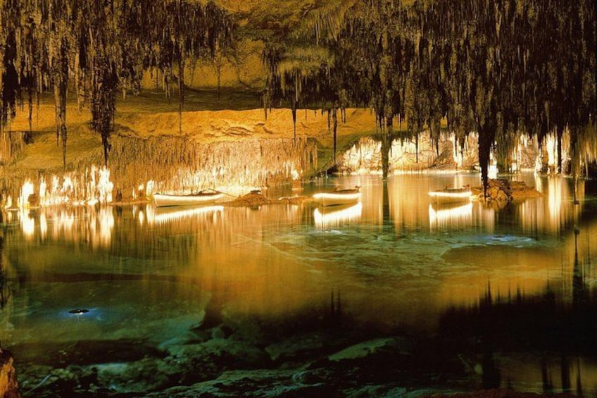 A cave with stalactites, a calm lake, and boats. 1