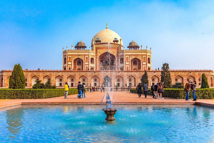 A large building with a central dome and four smaller domes, surrounded by a water fountain and a crowd of people. 1