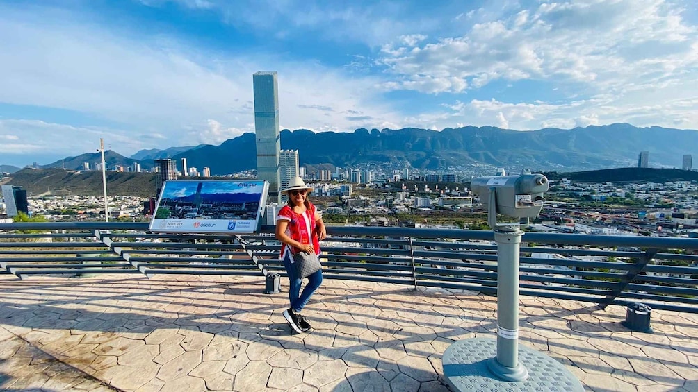 A person standing on a viewing platform with a cityscape and mountains in the background. 2