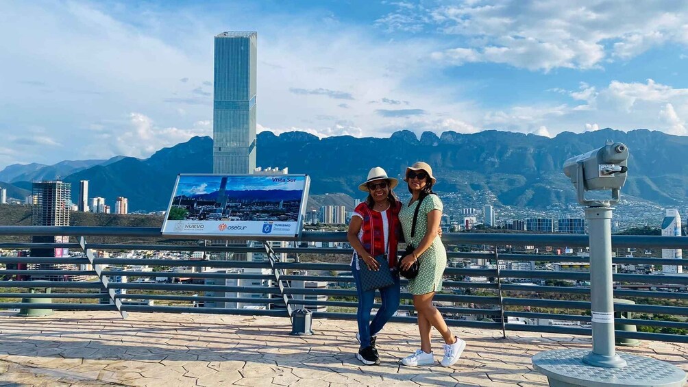 Two people standing on a viewing platform with a cityscape and mountains in the background. 4