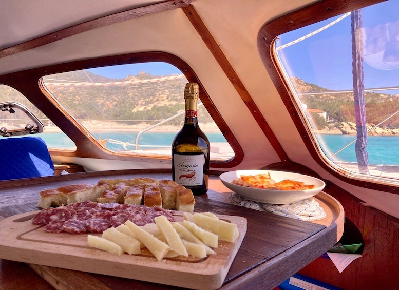 A boat interior with a wooden table displaying a bottle of wine, charcuterie, and a bowl of pasta. 5