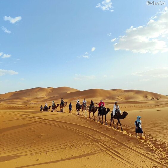 A group of people riding camels across a desert landscape with sand dunes. 1
