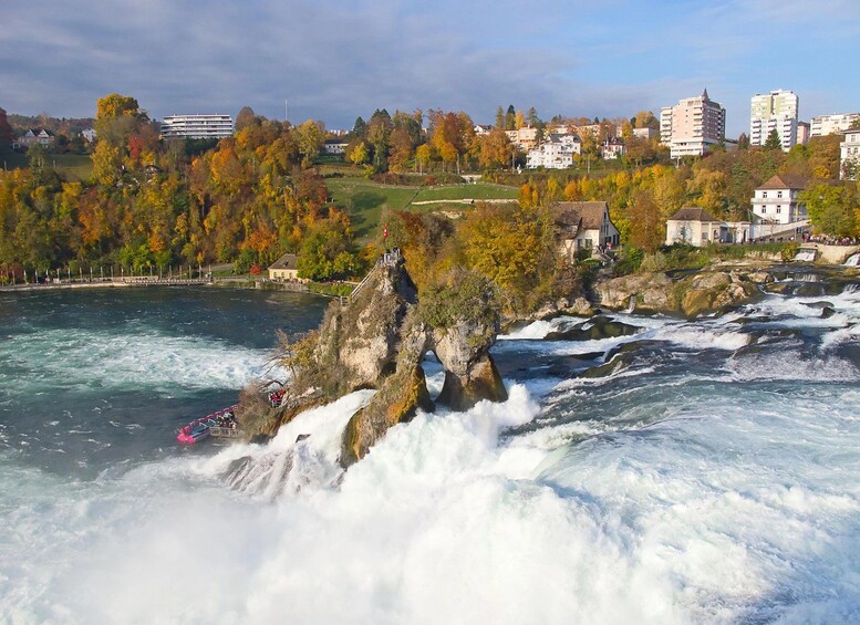 A river with a rocky outcrop, a boat, and buildings in the background. 1