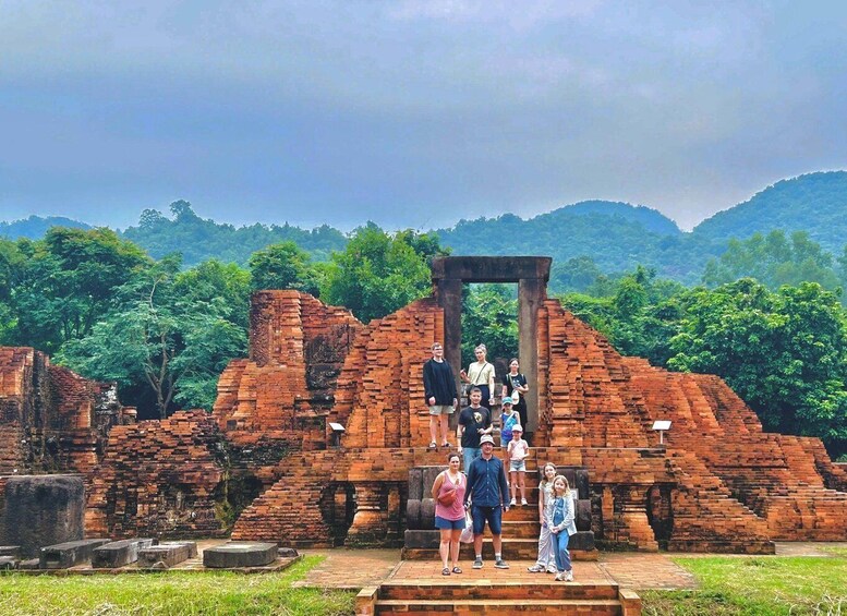 A group of people standing in front of ancient brick ruins with a forested mountain backdrop. 5