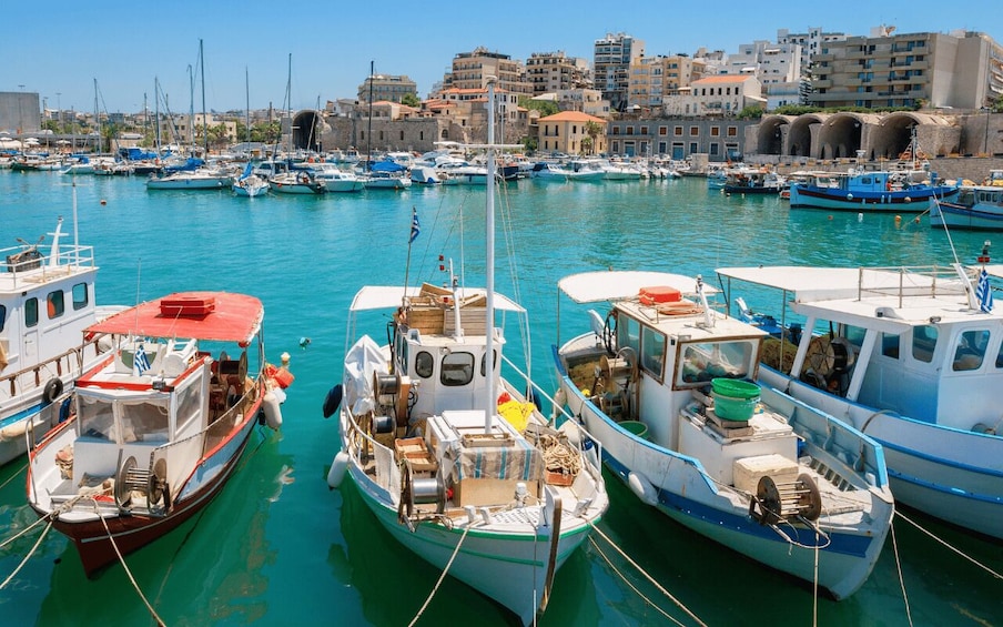 A marina with several boats docked, a clear blue sky, and buildings in the background. 1