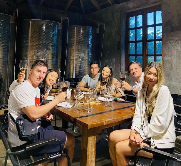 A group of people sitting around a wooden table in a rustic setting with metal tanks in the background. 5