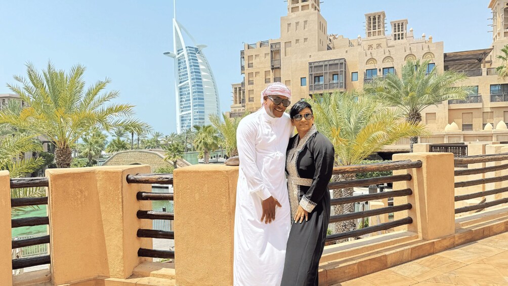 A man and woman standing on a bridge with palm trees and a modern building in the background. 2