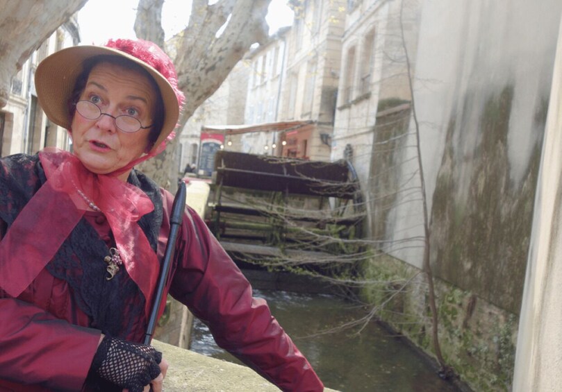 A person in historical attire near a canal with buildings and a bridge in the background. 4