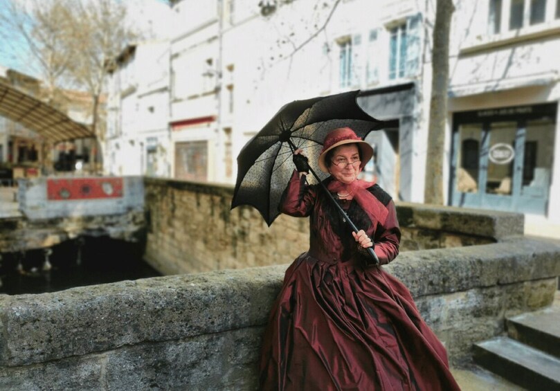 A person in a red dress holding an umbrella, standing by a stone wall in an urban setting. 2