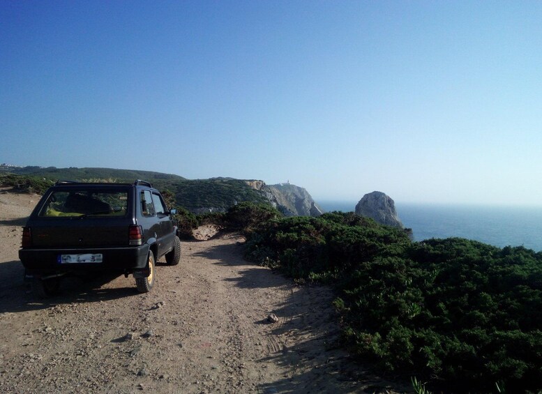 A parked SUV on a dirt path with a coastal landscape in the background. 3