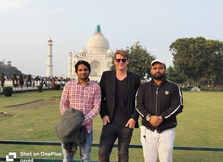 Three people standing in front of the Taj Mahal with a crowd in the background. 2