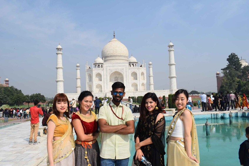 A group of people standing in front of the Taj Mahal with a pool in the foreground. 4