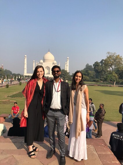Three people posing in front of the Taj Mahal with a park and trees in the background. 3