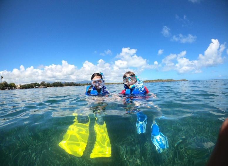 Two people snorkeling in clear blue water with a tropical landscape in the background. 2