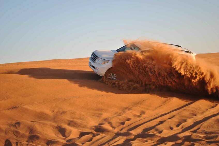 A white SUV driving through a desert with sand dunes. 4