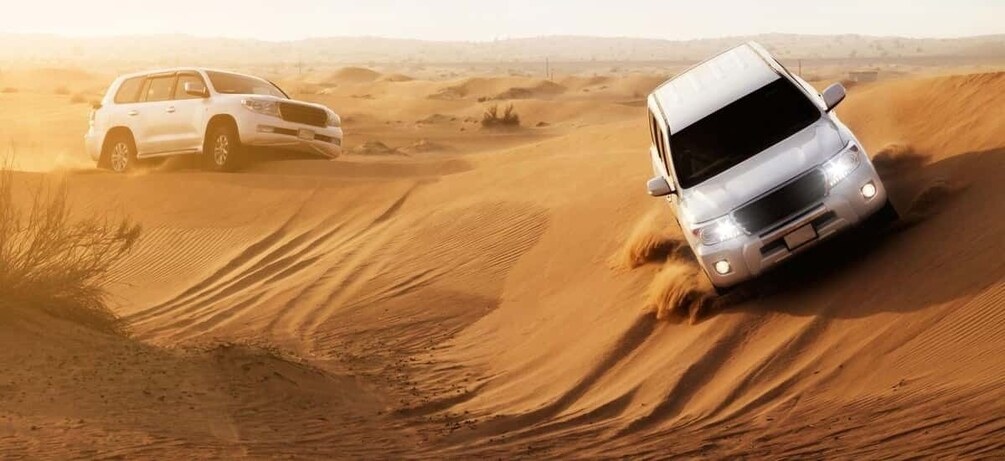 A white SUV navigating a sandy dune in a desert landscape. 2