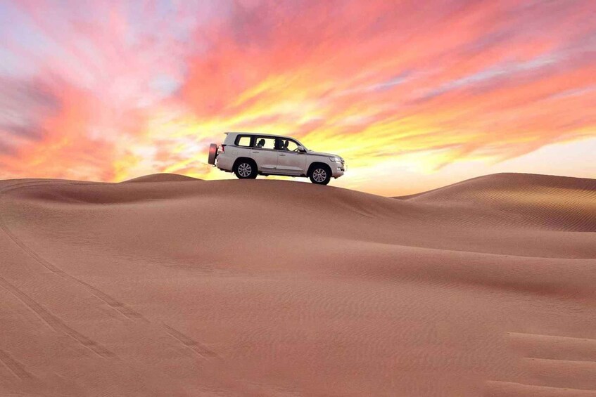 A white SUV driving across sand dunes with a colorful sunset in the background. 3