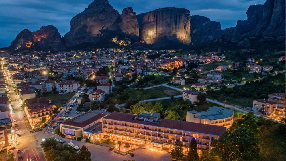 A city at dusk with illuminated buildings and a prominent mountain range in the background. 2