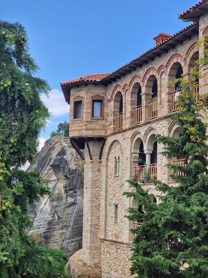 A historic stone building with arched windows and balconies, surrounded by lush greenery and a rocky cliff. 5