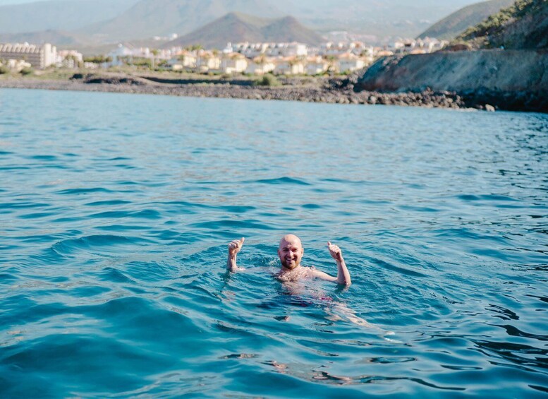 A person swimming in a body of water with a coastal town and mountains in the background. 5